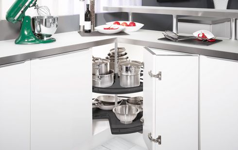 Weiße Eckküche mit offenem Schrank, drehbarem Regal mit Töpfen, Schüsseln und Küchenmaschine auf der Arbeitsplatte.